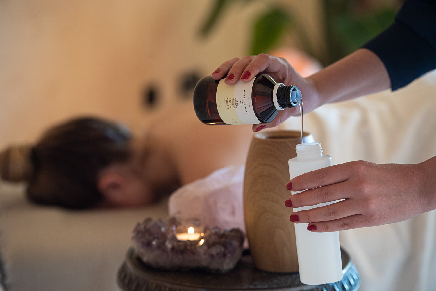Relax Master minerale olie wordt in een fles gegoten naast een Relax master massage olieverwarmer houtlook in een massagesalon met een sfeervolle kaars